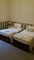 Dos camas individuales con sábanas y almohadas blancas, una mesita de noche con lámpara y un teléfono.