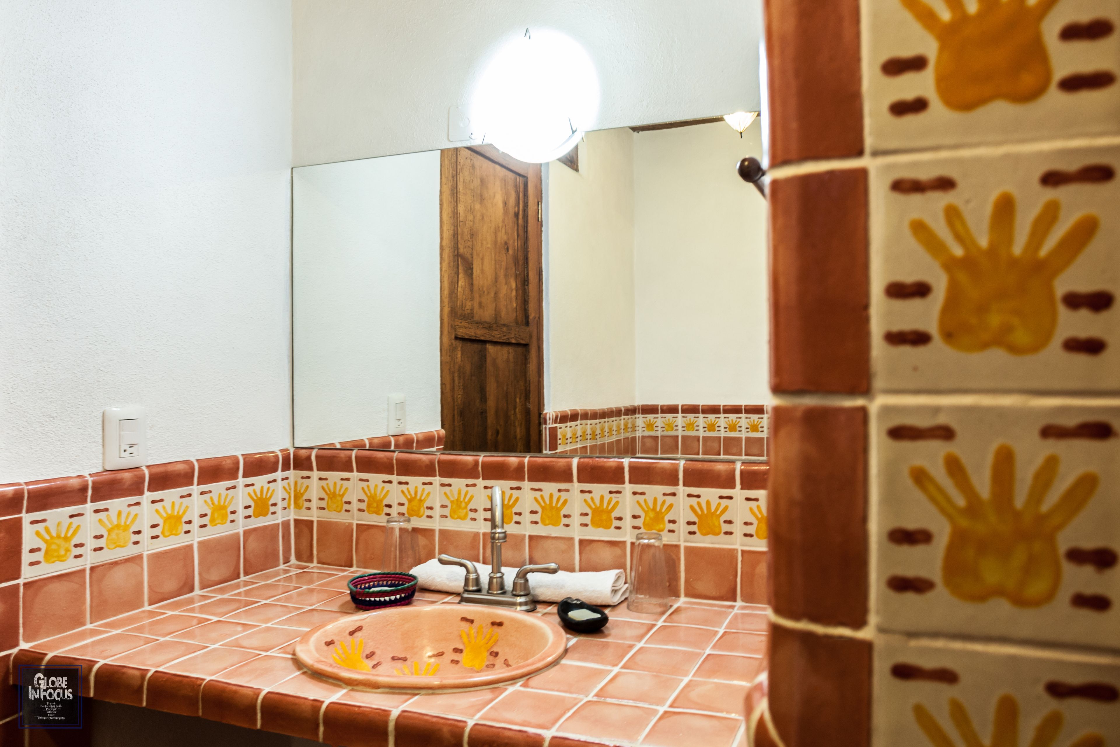Un baño con lavamanos, espejo y azulejos pintados a mano.