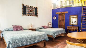 Una habitación con dos camas, una mesa de madera, un balcón y una pared azul.