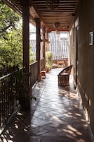Un corredor al aire libre cubierto con suelo de baldosas, columnas de madera y plantas en macetas.