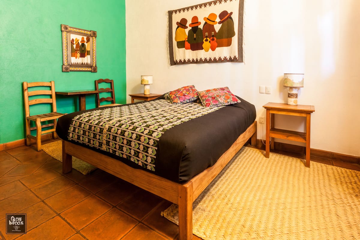 A room with a wooden bed, two chairs, a small table, and a lamp.