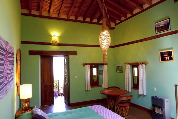 A room with a bed, a table, chairs, a hanging light fixture, and a door leading to an outdoor area.