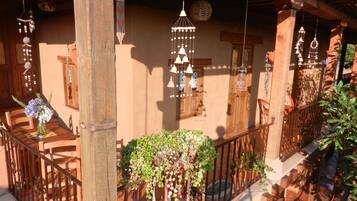 Varanda de madeira com chimes de vento pendurados, guarda-corpo de madeira e vasos de plantas.