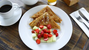Une assiette de petit-déjeuner avec des toasts, des fraises et du melon, posée sur une table en bois.