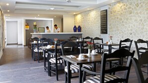 Un restaurant avec des tables et des chaises en bois, un espace d’accueil et un mur en pierre.