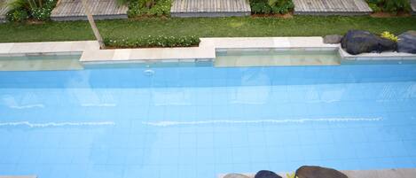 A swimming pool with a wooden deck, surrounded by rocks and plants.