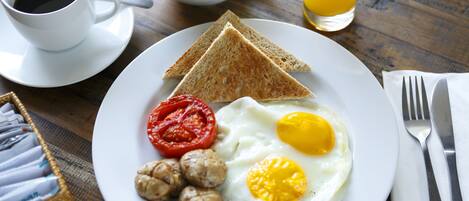 A breakfast plate with toast, eggs, tomatoes, and sausages on a wooden table.