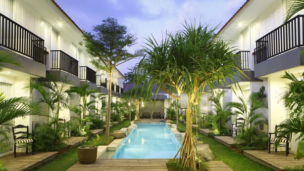 Un espace piscine avec des chaises longues, une terrasse en bois et un petit jardin agrémenté de palmiers.