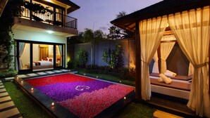 A modern hotel with a well-lit outdoor area featuring a flower bed, a balcony with plants, and a cozy seating area with a canopy. - Agata Villas (Seminyak)