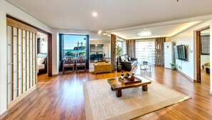 Un salón espacioso con suelo de madera, un sofá grande, una mesa de centro y vistas a la ciudad a través de amplios ventanales.