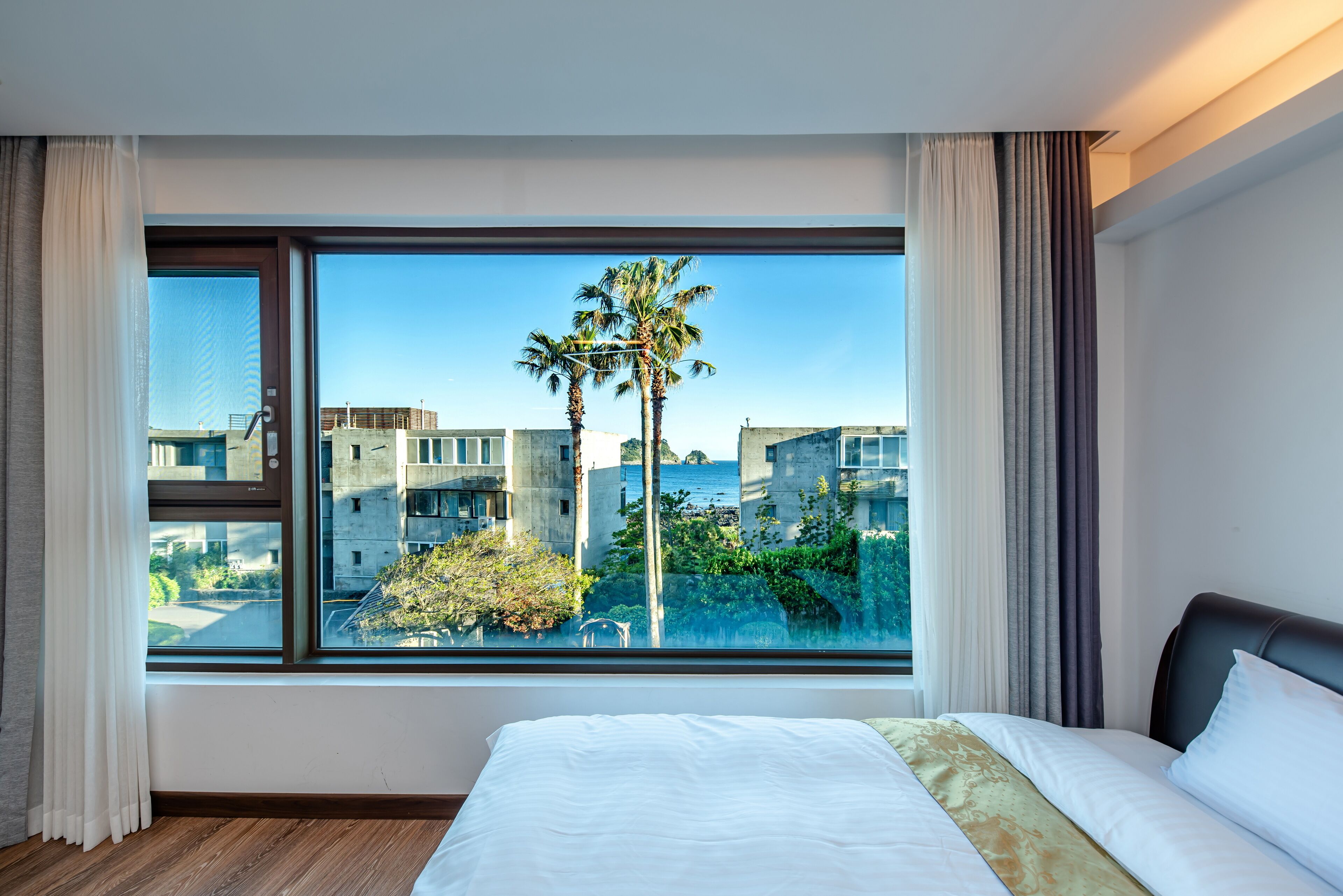 A hotel room with a large window offering a view of palm trees and buildings.