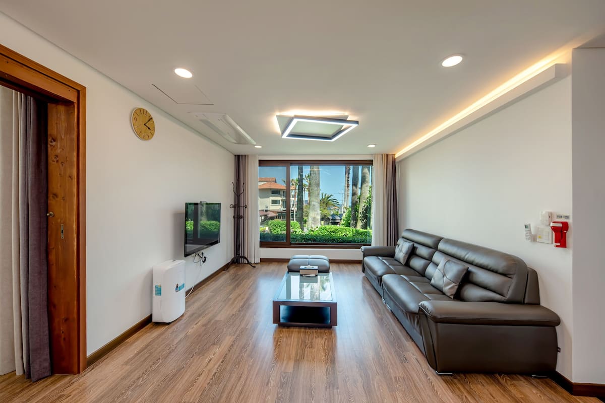 A modern living room with a sofa, a coffee table, a TV, and a large window with a view of greenery.