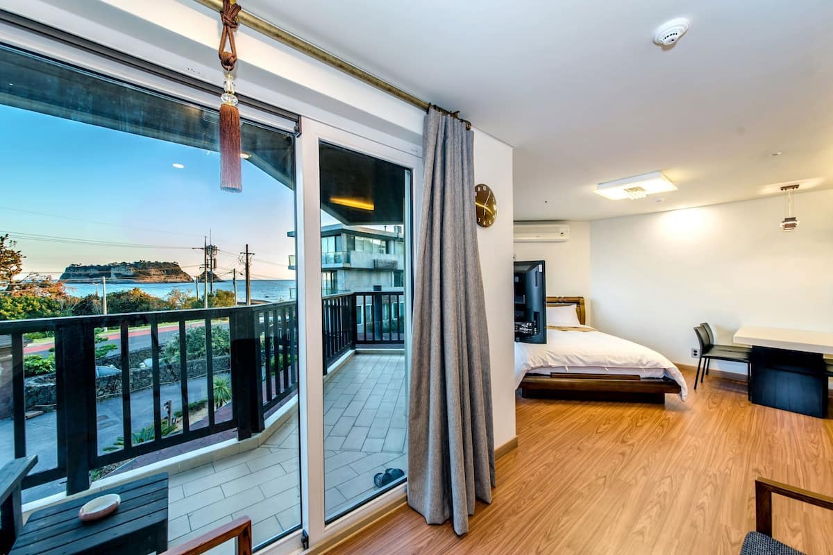 A modern hotel room with a balcony, a bed, a desk, and a TV.