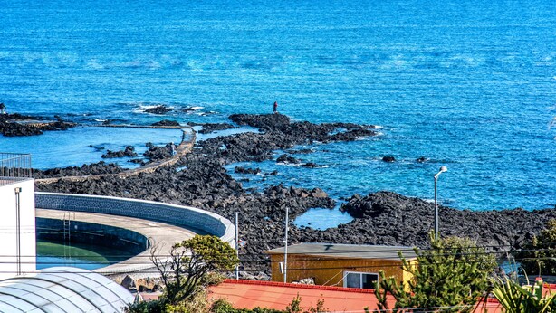Vista costera con piscina, costa rocosa y un edificio de techo rojo.