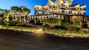 Un hotel de varios pisos con balcones, palmeras y un camino de acceso bien iluminado.