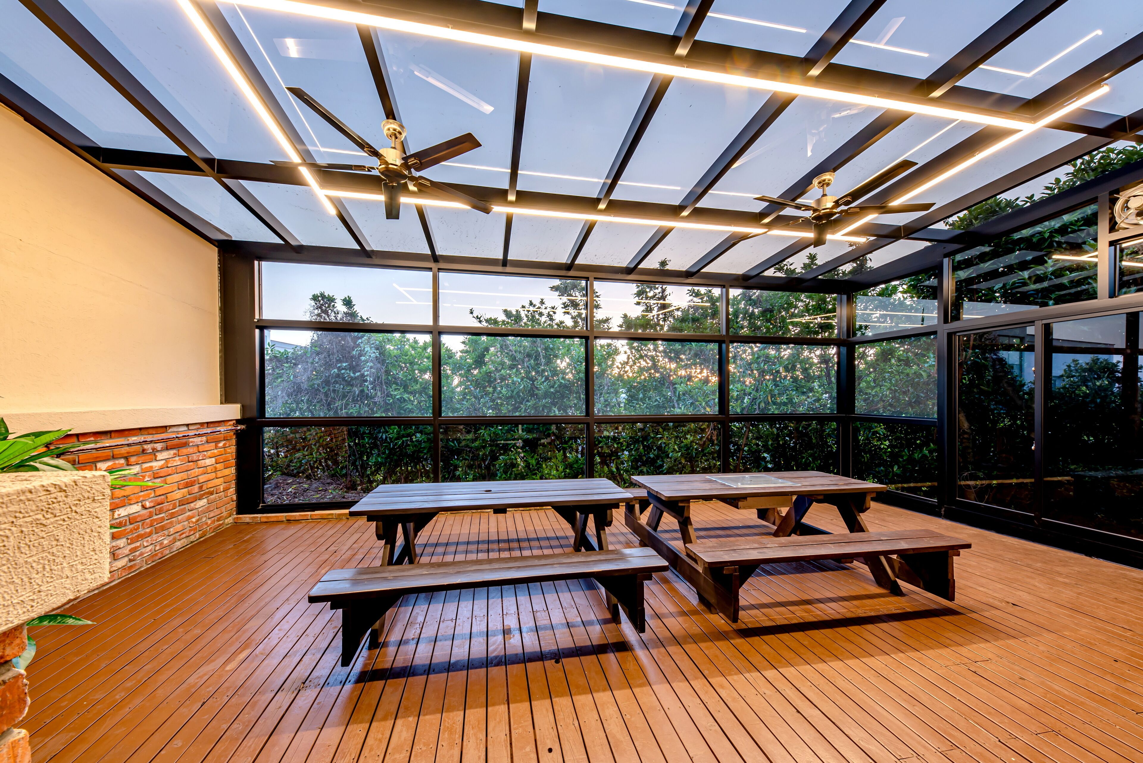 Un espace extérieur abrité, doté de tables de pique-nique en bois, de grandes fenêtres et de ventilateurs de plafond.