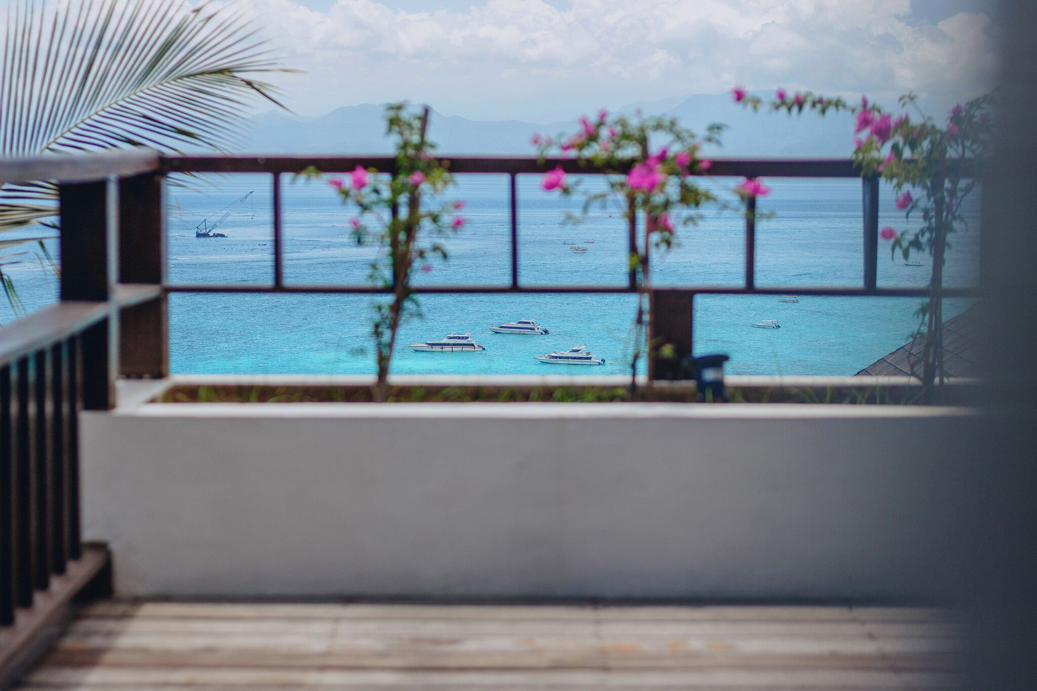 A balcony with a view of the sea, featuring boats and a mountainous backdrop.