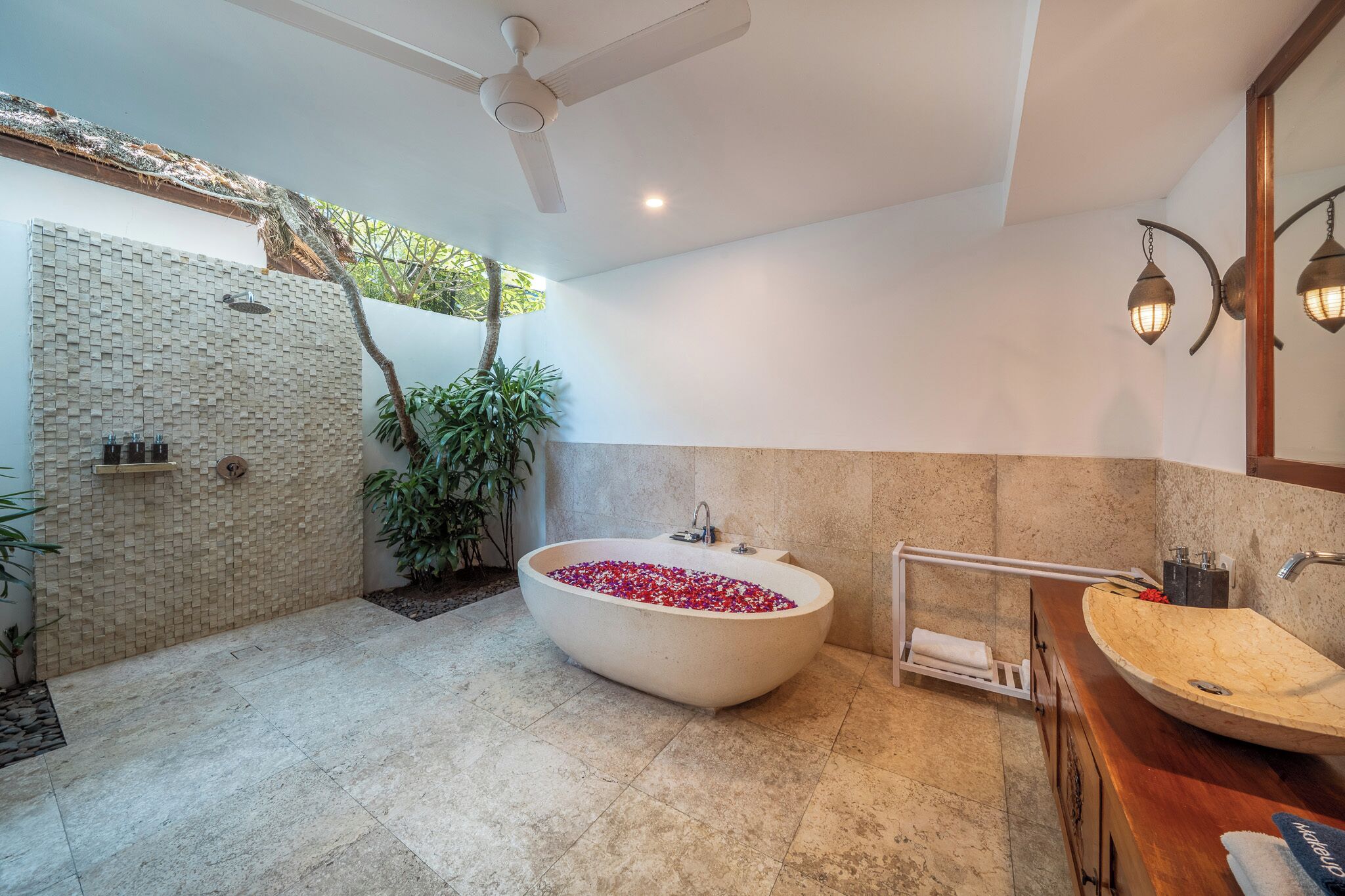 Une salle de bain moderne avec une baignoire îlot remplie de pétales de roses, un grand miroir et un meuble-lavabo en bois.