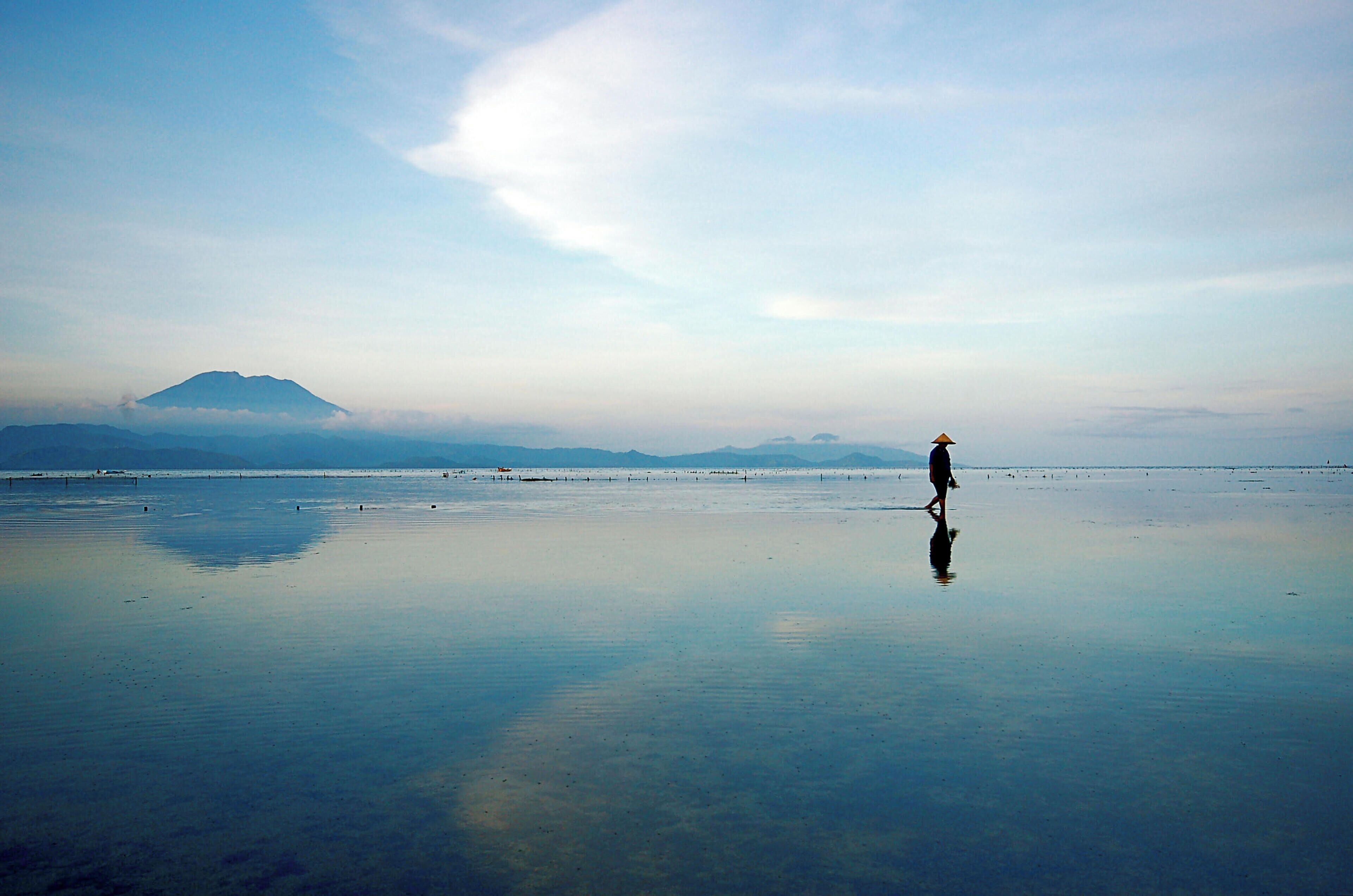 Una playa tranquila con una persona caminando, una montaña al fondo y un cielo despejado.