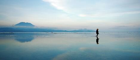 Una playa tranquila con una persona caminando, una montaña al fondo y un cielo despejado.