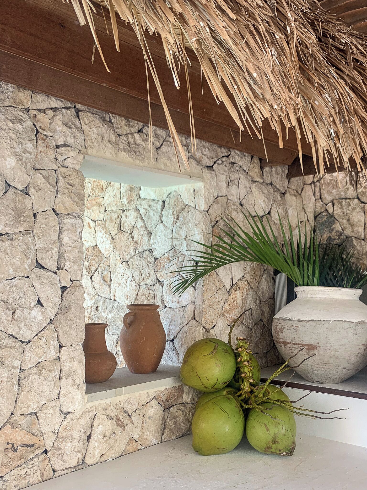 A stone wall with a shelf holding pottery and coconuts.