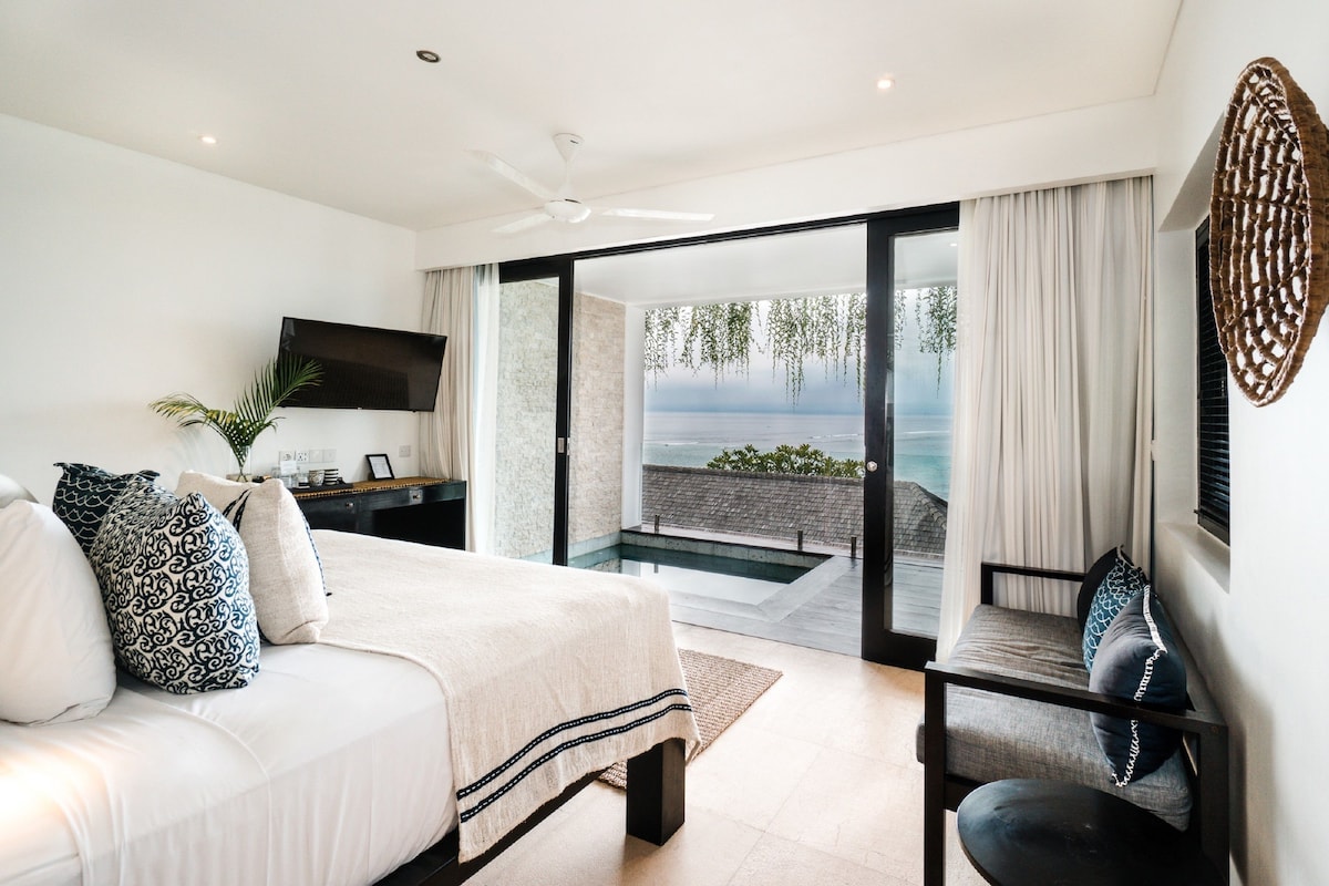 Un dormitorio con cama, televisor, escritorio y vistas al océano.