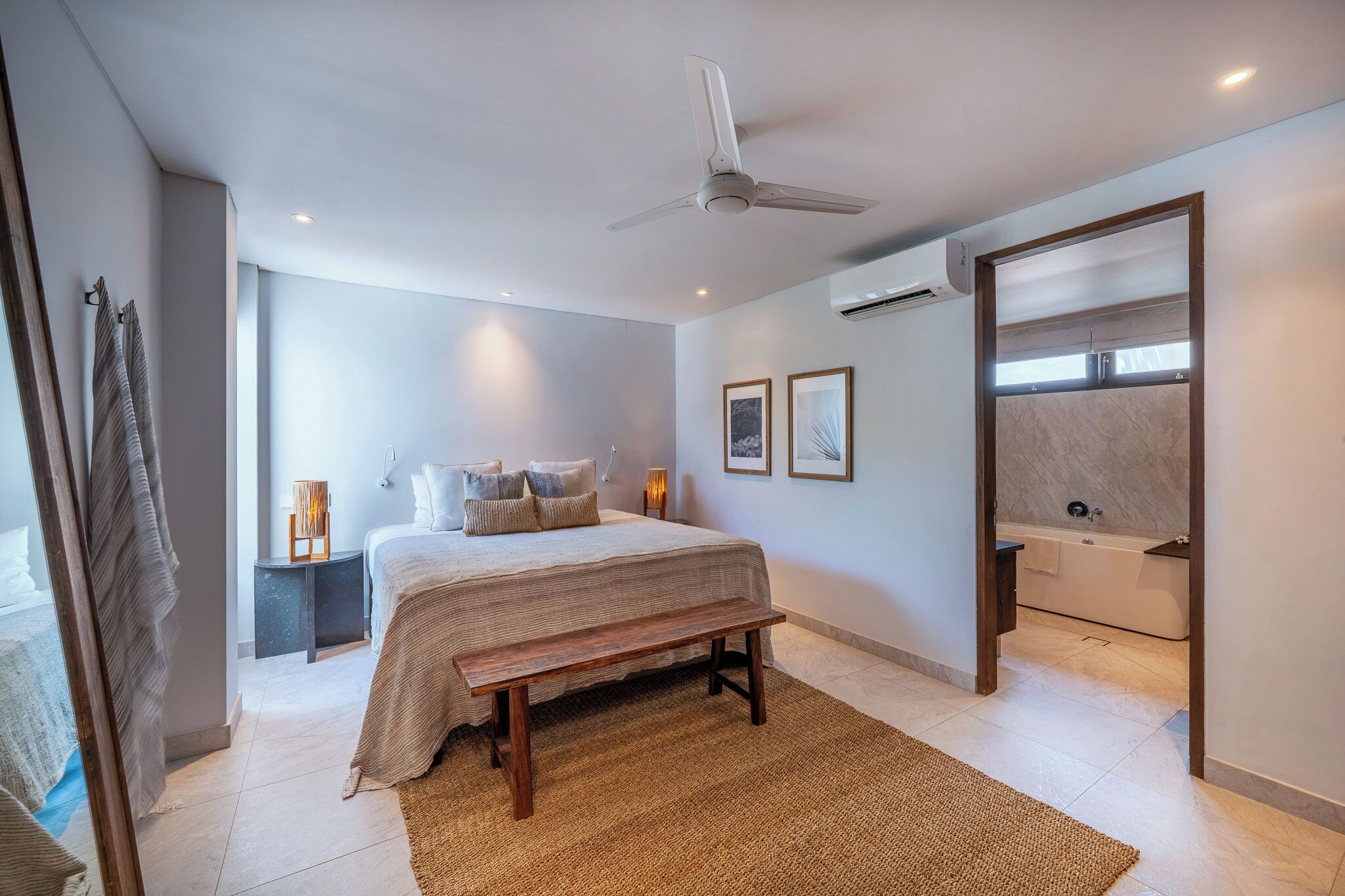 Un dormitorio con cama, un banco, una mesita de noche y un baño con bañera.