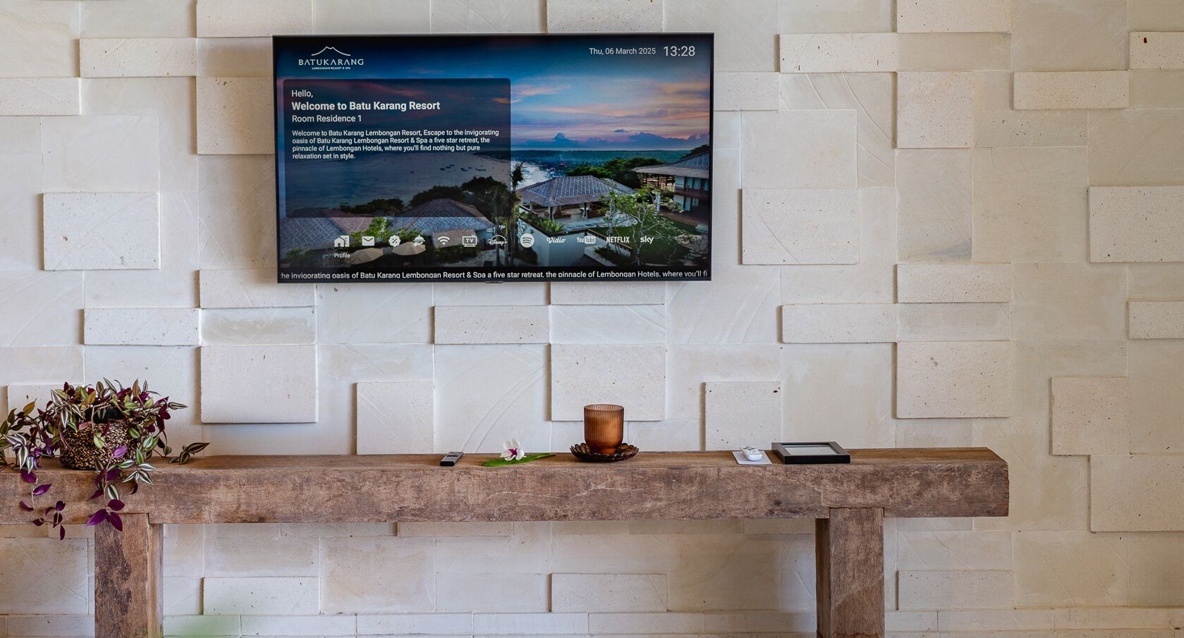 Mostrador de recepción en Batu Karang Resort con un mensaje de bienvenida, un teléfono inteligente, una vela y una planta en maceta.