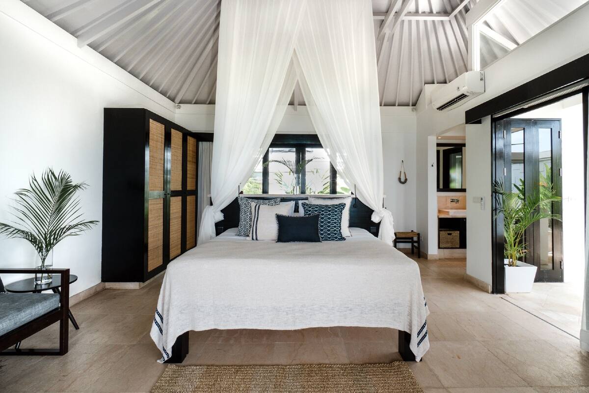 A spacious bedroom with a large bed, a sitting area with a chair and table, and a view of the outdoors.