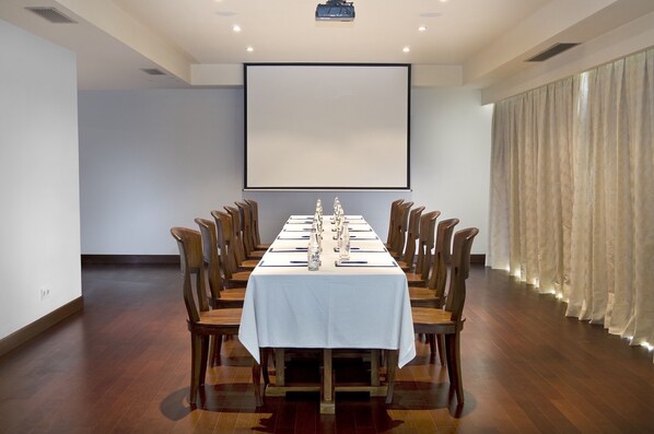 A conference room with a long table, wooden chairs, a projector screen, and a curtain. - Batu Karang Lembongan Resort & Spa (Lembongan Island)