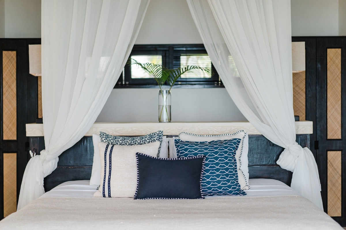 Una cama con dosel, un florero con una planta y una ventana con persianas.