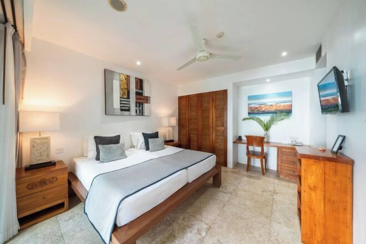 A bedroom with a bed, bedside tables, a desk, a chair, a TV, and artwork on the walls.