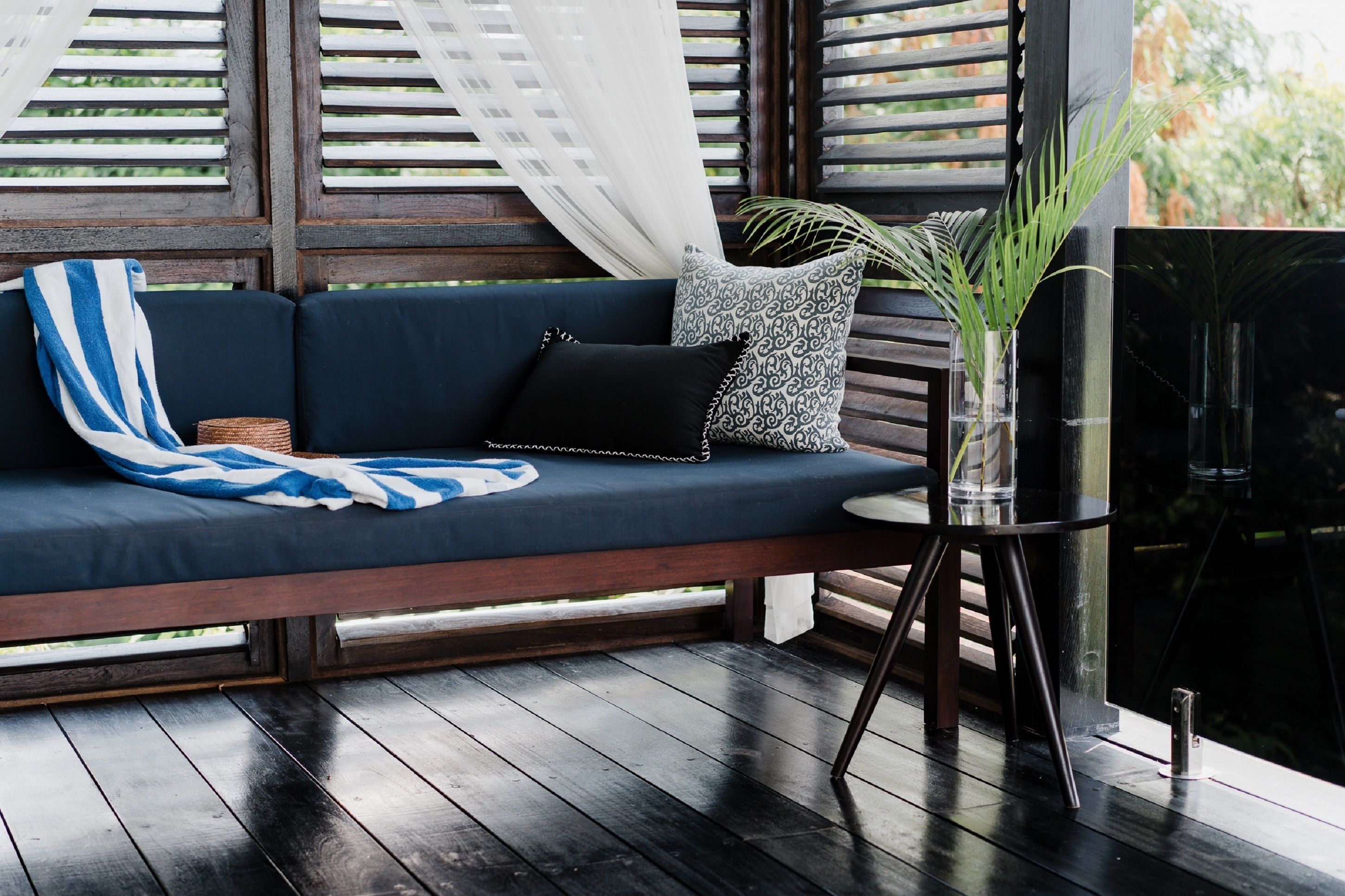 A dark wooden deck with a blue sofa, a small round table, and a black TV on a stand.