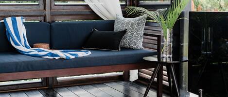 A dark wooden deck with a blue sofa, a small round table, and a black TV on a stand.