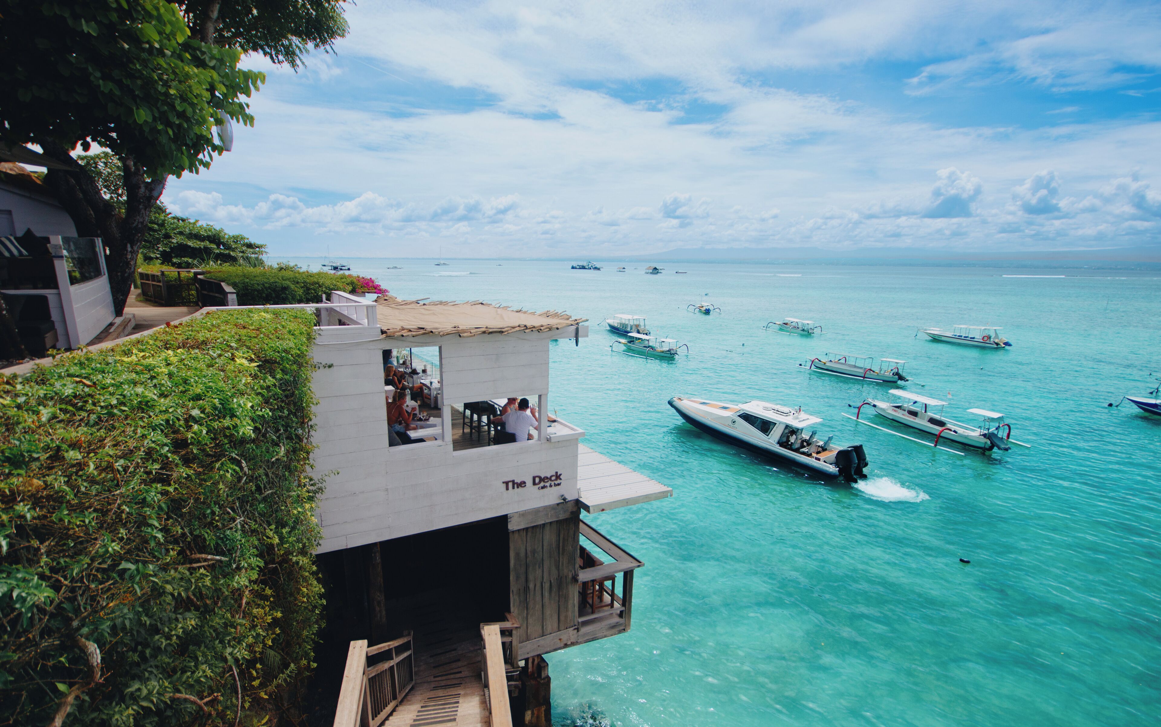 A waterfront property with a deck overlooking turquoise waters, boats, and a lush green landscape.
