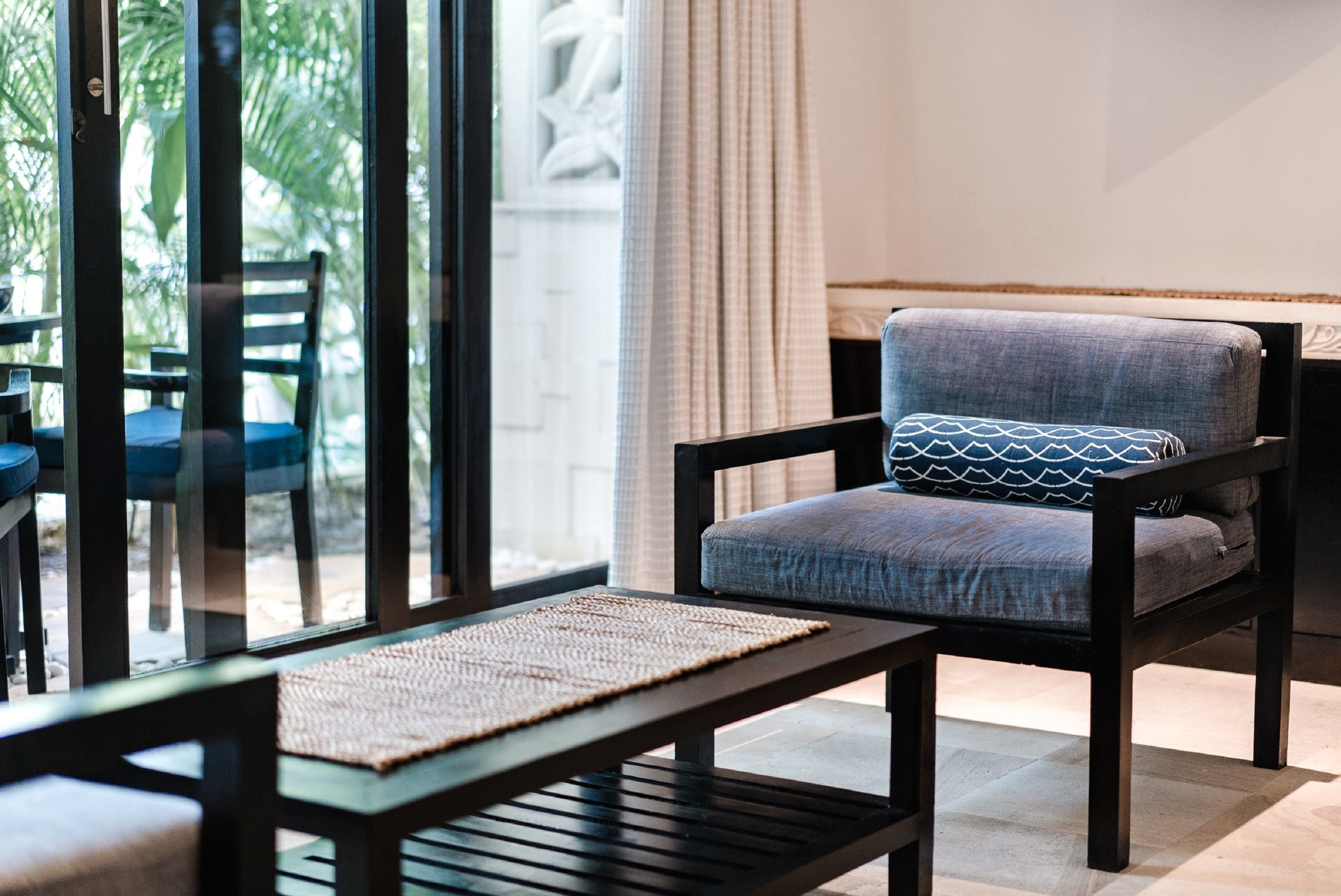 A modern room with a dark wooden chair, a matching ottoman, and a woven mat on a wooden table.