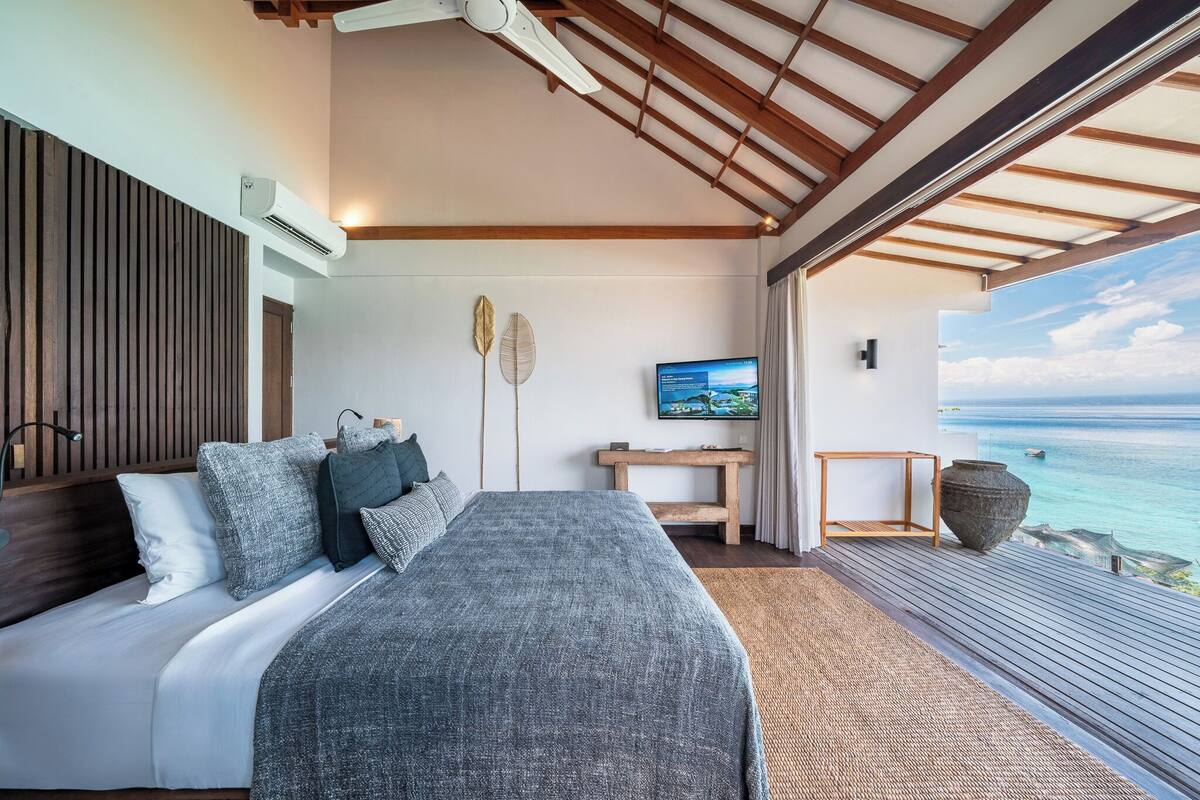 A bedroom with a bed, a TV, and a view of the ocean.
