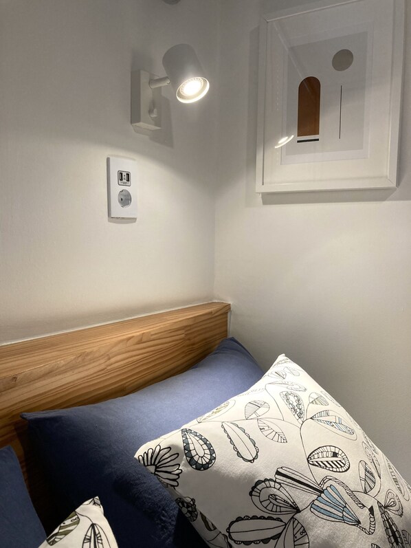 A bedroom with a wooden headboard, a single bed with a patterned pillow, a wall-mounted light, and a power outlet. - Hostel Beige 2nd (Seoul)