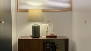 A corner with a wooden console table, a lamp, a framed picture, and a window with blinds. - Hostel Beige 2nd (Seoul)