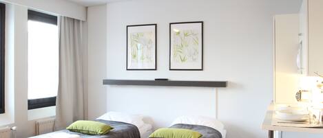 Habitación de hotel con dos camas, una mesita con un bol y una taza, y una ventana con cortinas.