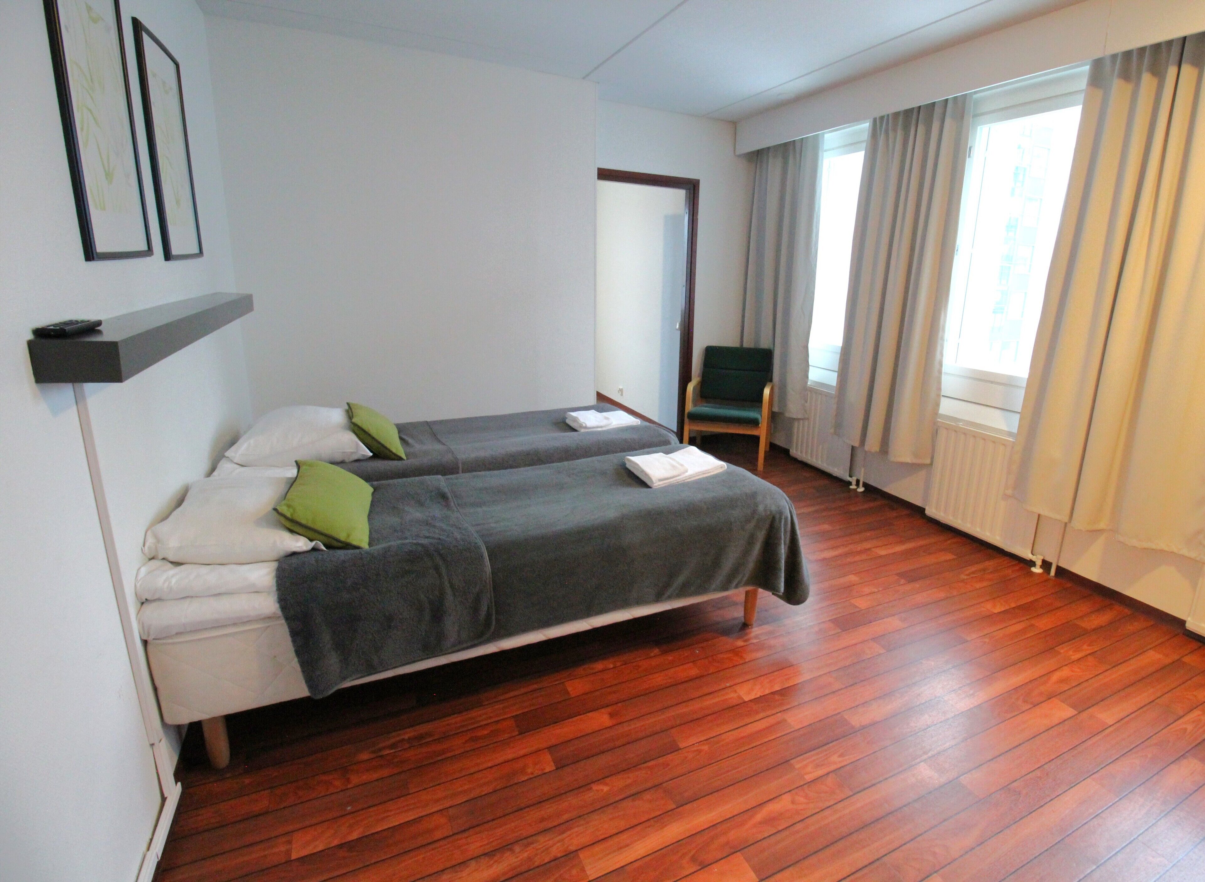 A room with two beds, a chair, a window with curtains, and a radiator.