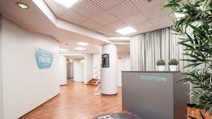 Ein moderner Empfangsbereich mit Holzboden, einem Empfangstresen mit der Aufschrift „RECEPTION“ und einem Schild für „APARTHOTEL FORENOM“.