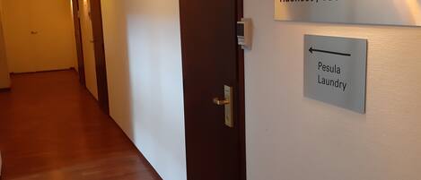 Un couloir d’hôtel avec un plancher en bois, une porte portant le numéro « 703 » et un panneau indiquant « Huoneet / chambres 701-717 » et « Pesula, laverie ».