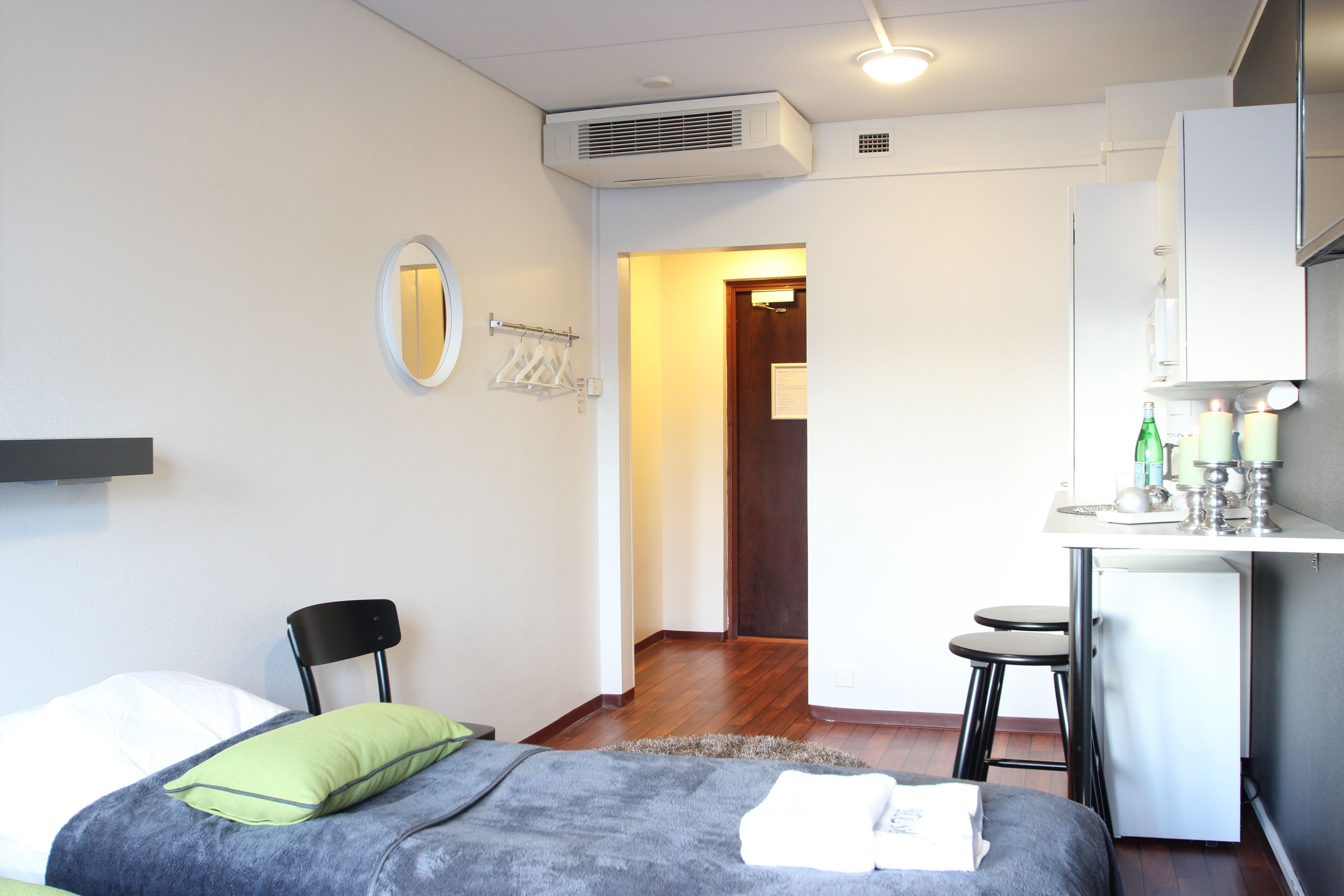 Een kleine kamer met een bed, een stoel, een kitchenette en een spiegel.