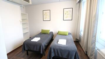 A room with two single beds, a white air conditioning unit, a white radiator, and two framed botanical prints on the wall.