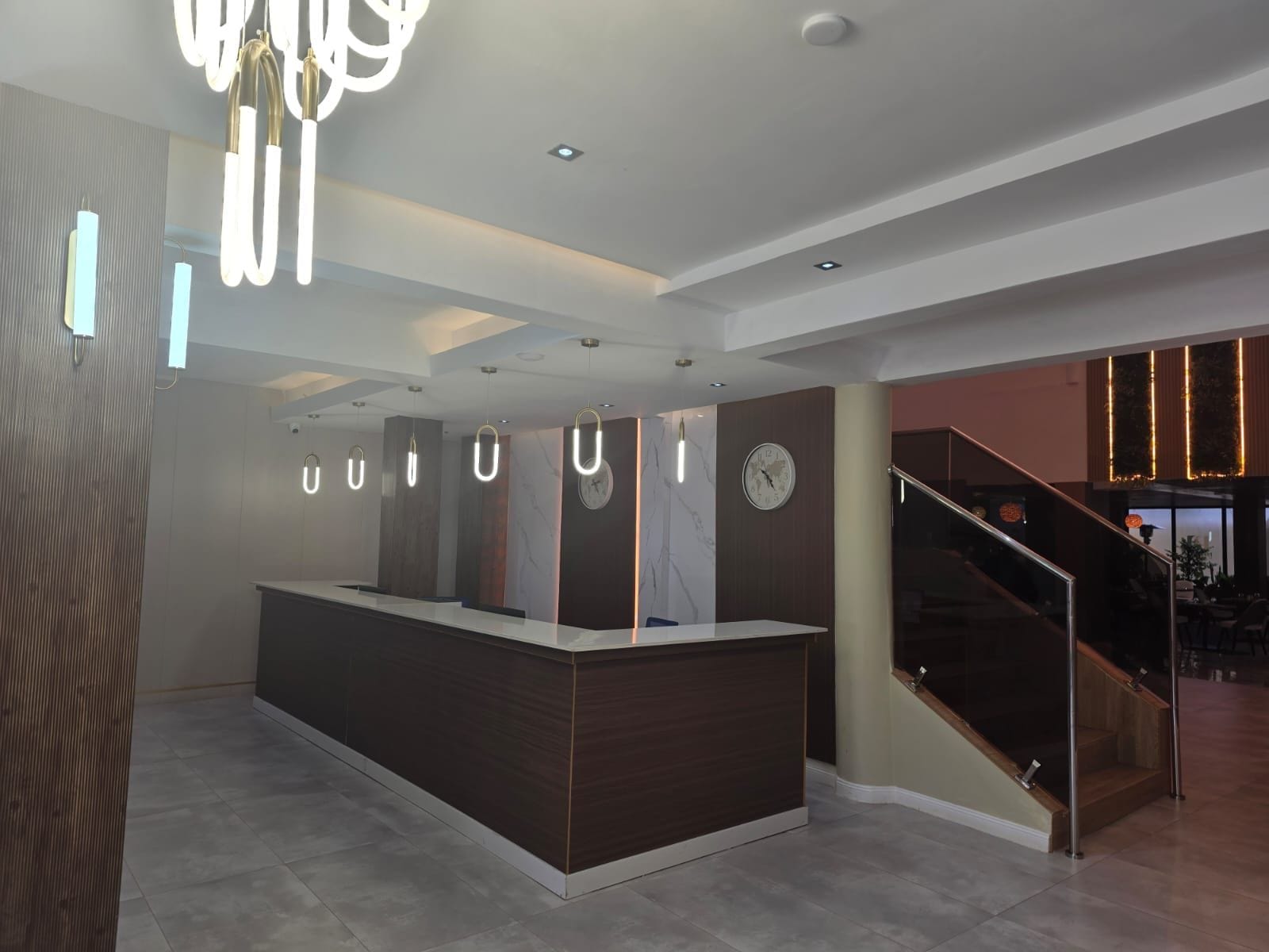 Un área de recepción moderna con un mostrador central, un reloj y una escalera que lleva a un nivel superior.