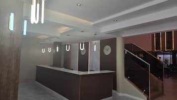 Un área de recepción moderna con un mostrador central, un reloj y una escalera que lleva a un nivel superior.