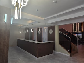 A modern reception area with a central desk, a clock, and a staircase leading to an upper level. - Park Place Hotel (Nairobi)