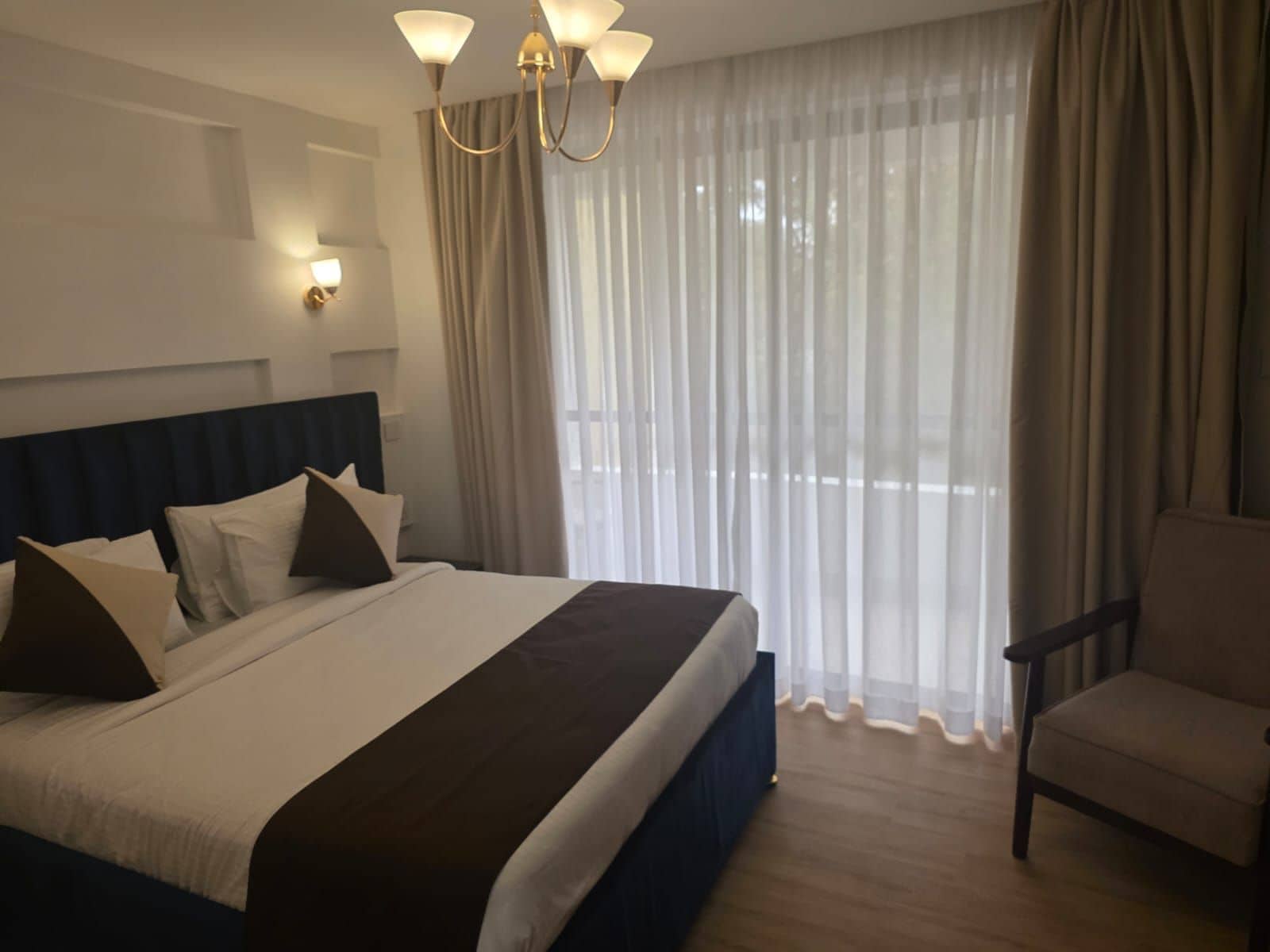 Habitació d'hotel amb un llit gran, una cadira, un penjallum i cortines translúcides.