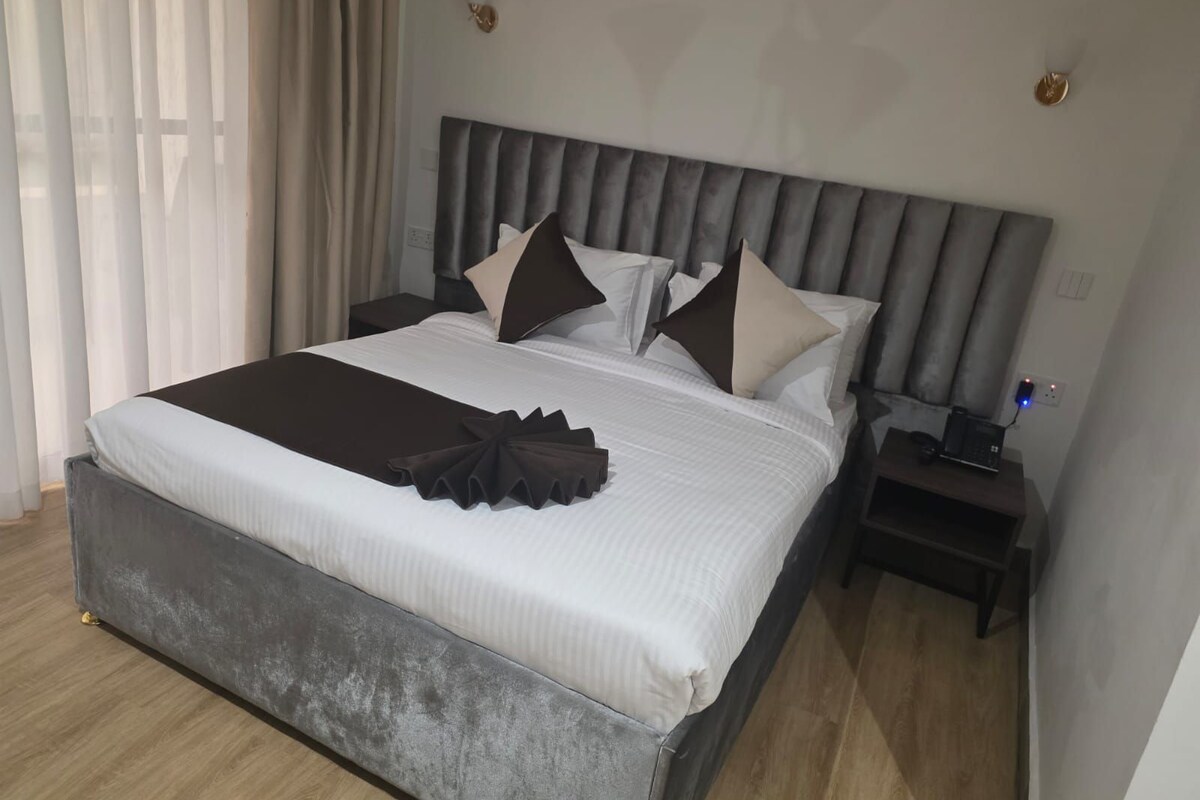 A hotel room with a large bed, a bedside table with a lamp, and a power outlet.